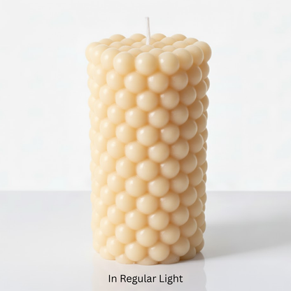 Beige glow in the dark bubble-textured pillar candle on a white background in regular light
